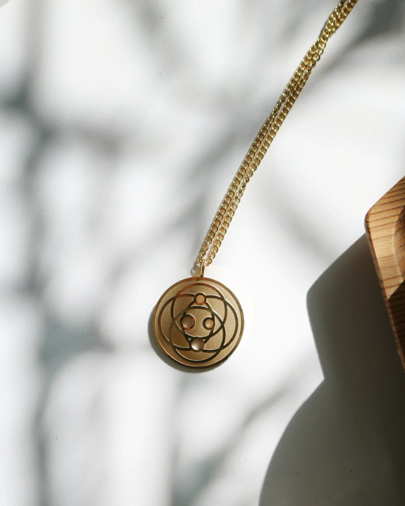 Gold Harmoni Pendant on its chain in dappled sunlight