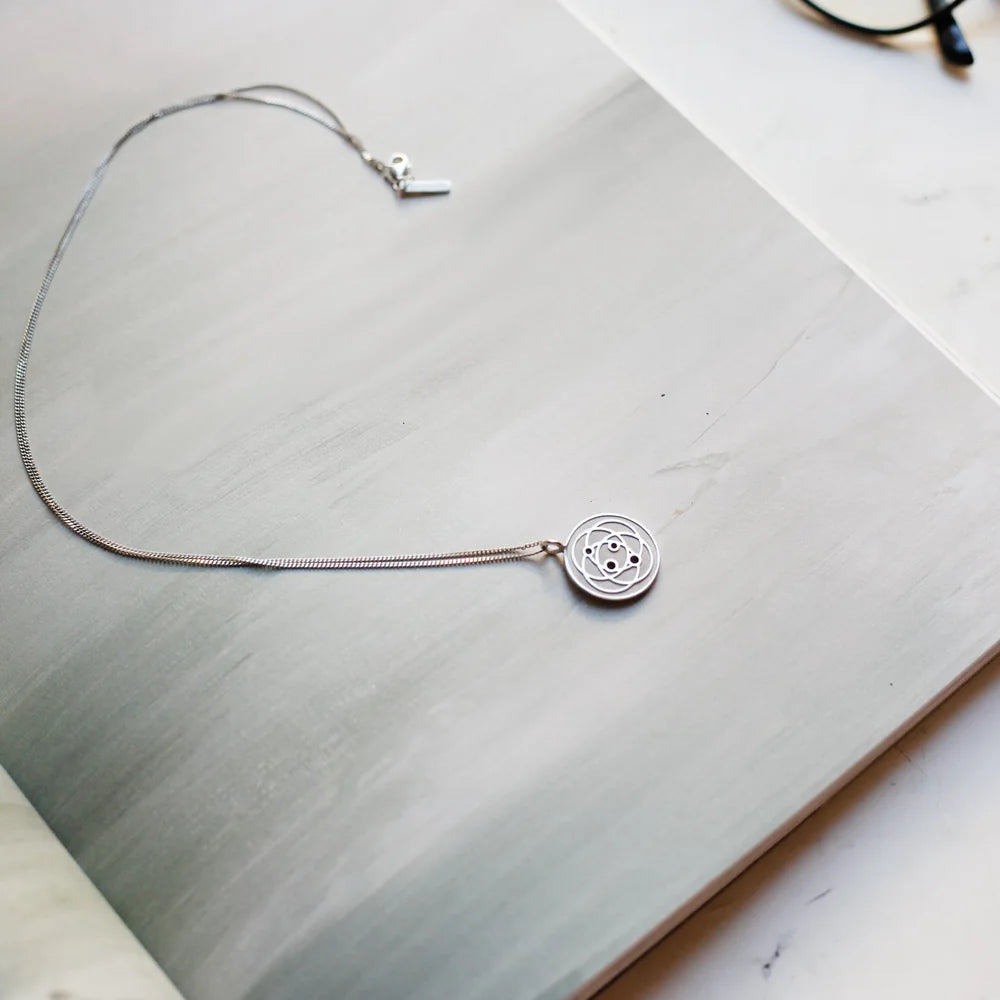 Stainless Harmoni Pendant on its chain resting on white marble