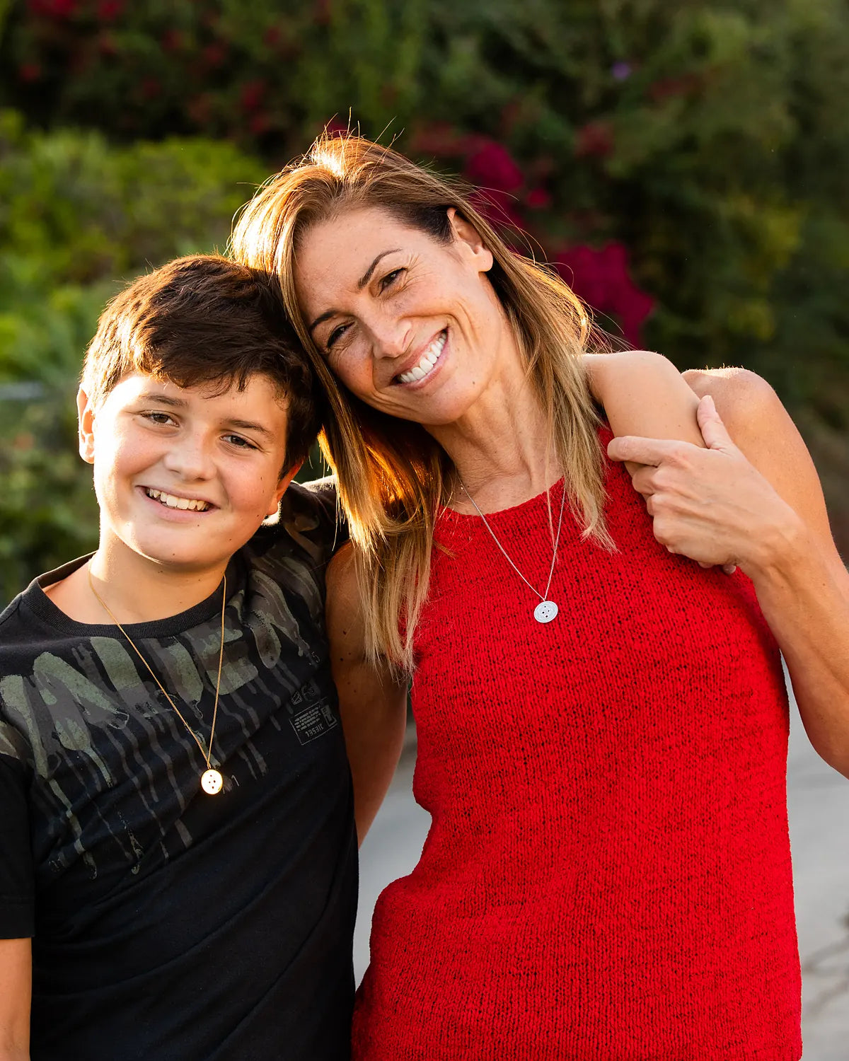 Smiling mother and teenage son outdoors, she wears a stainless Harmoni Pendant and he wears a gold one
